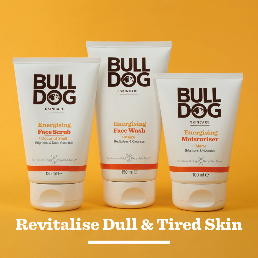 The Energising Face Scrub from Bulldog Skincare is shown against a yellow background with the text “Revitalise Dull & Tired Skin” at the bottom, highlighting its natural origin ingredients.