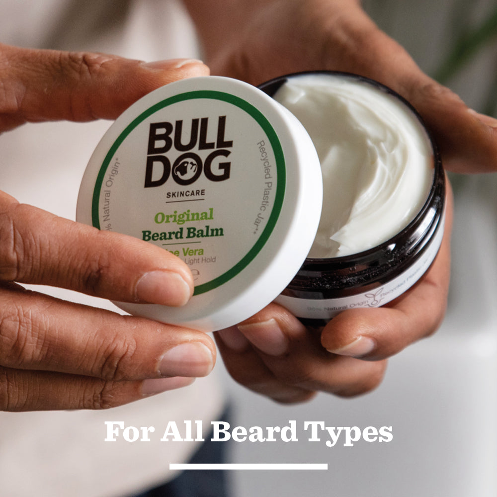 Someone opens a jar of Original Beard Balm, revealing a creamy white formula made with natural origin ingredients. The words For All Beard Types appear at the bottom of the image.