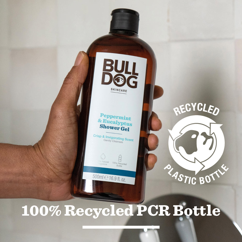 A hand holds a bottle of Peppermint & Eucalyptus Shower Gel featuring a 100% recycled PCR plastic bottle with recycling symbol, offering an invigorating cleanse and natural fragrance.