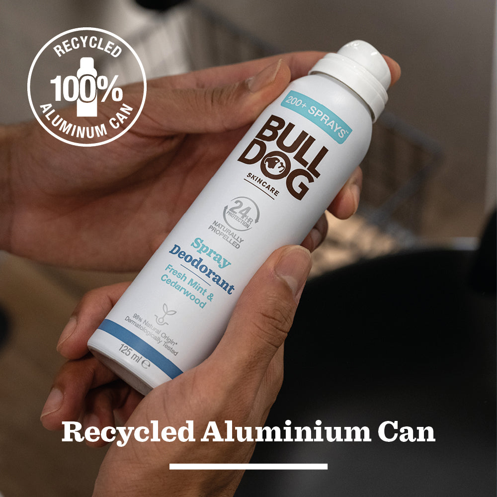 Someone holds a Fresh Mint & Cedarwood Spray Deodorant can from Bulldog Skincare, labeled “Recycled 100% Aluminium Can,” featuring natural origin ingredients and a vegan formula.