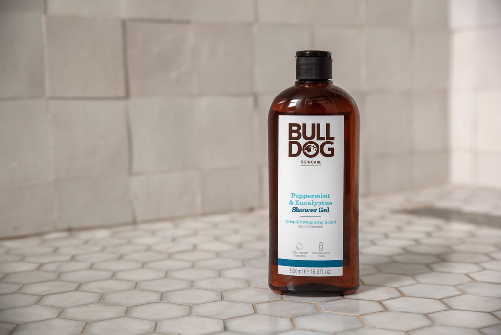 A bottle of Peppermint & Eucalyptus Shower Gel is displayed on white hexagonal tiles, delivering an invigorating cleanse with its natural fragrance against a tiled bathroom wall.